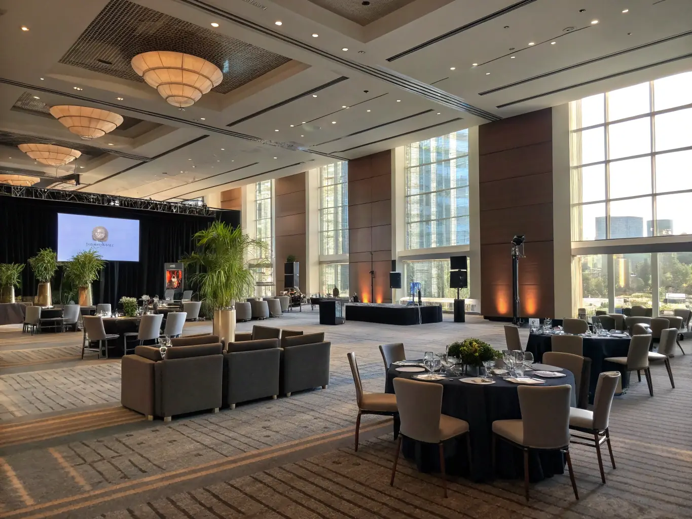 A modern conference hall filled with attendees listening to a keynote speaker on stage, with a large screen displaying the conference logo and presentation slides.